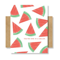 A watermelon-patterned greeting card with red watermelon slices on a white background and the phrase 'YOU'RE ONE IN A MELON.' printed near the bottom, shown with kraft paper envelopes on both sides against a light gray background.