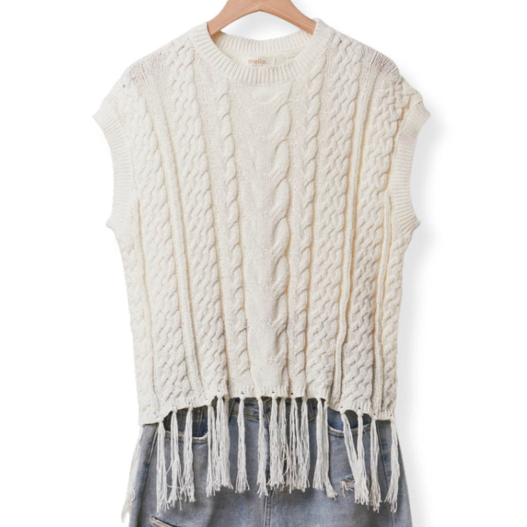 Cream cable-knit sleeveless sweater vest with fringe trim, hanging on a wooden hanger against a white background.
