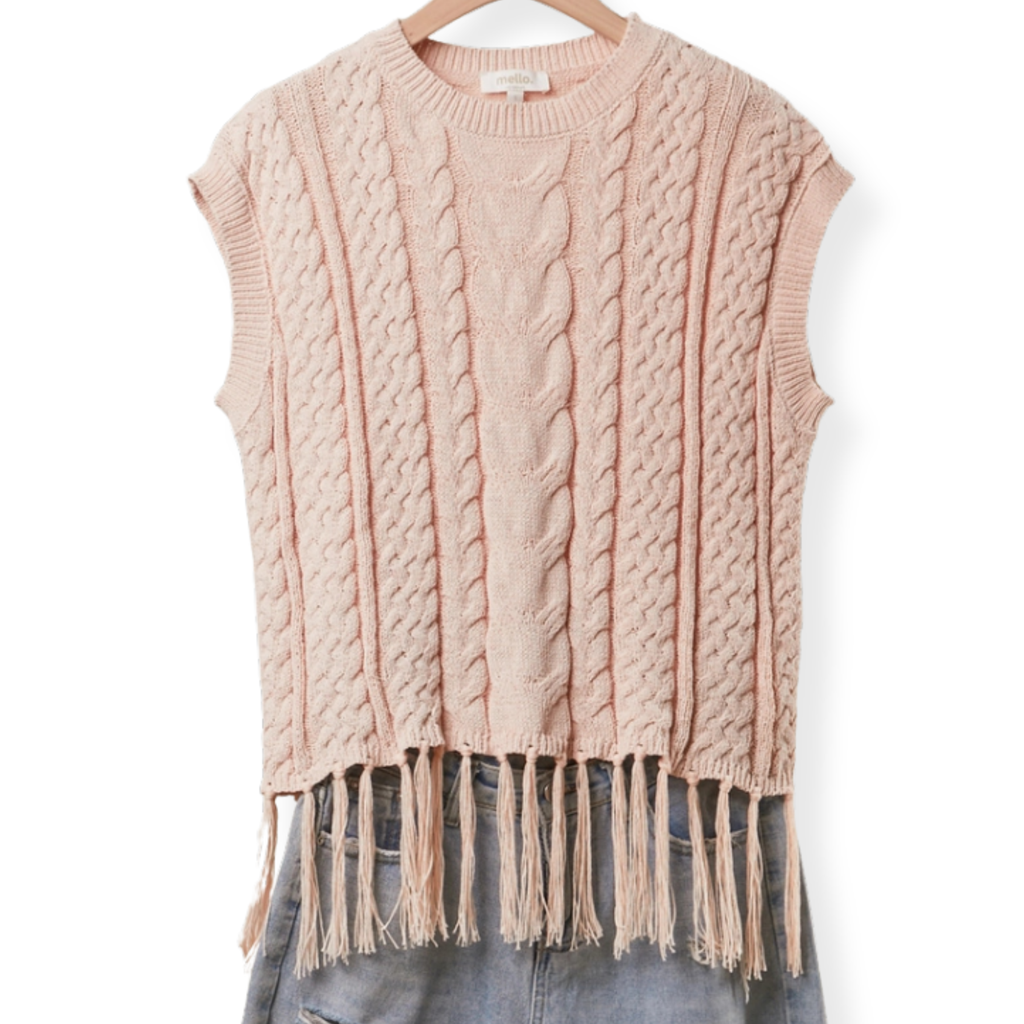 A sleeveless cable-knit sweater vest in a soft dusty pink color, featuring a crew neck and a fringed hem, displayed on a wooden hanger with blue jeans underneath against a white background.