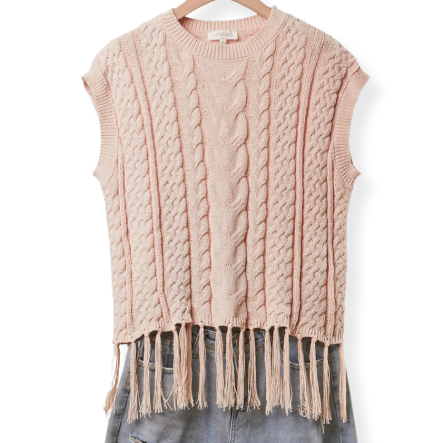 A sleeveless cable-knit sweater vest in a soft dusty pink color, featuring a crew neck and a fringed hem, displayed on a wooden hanger with blue jeans underneath against a white background.