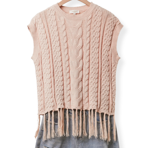 A sleeveless cable-knit sweater vest in a soft dusty pink color, featuring a crew neck and a fringed hem, displayed on a wooden hanger with blue jeans underneath against a white background.