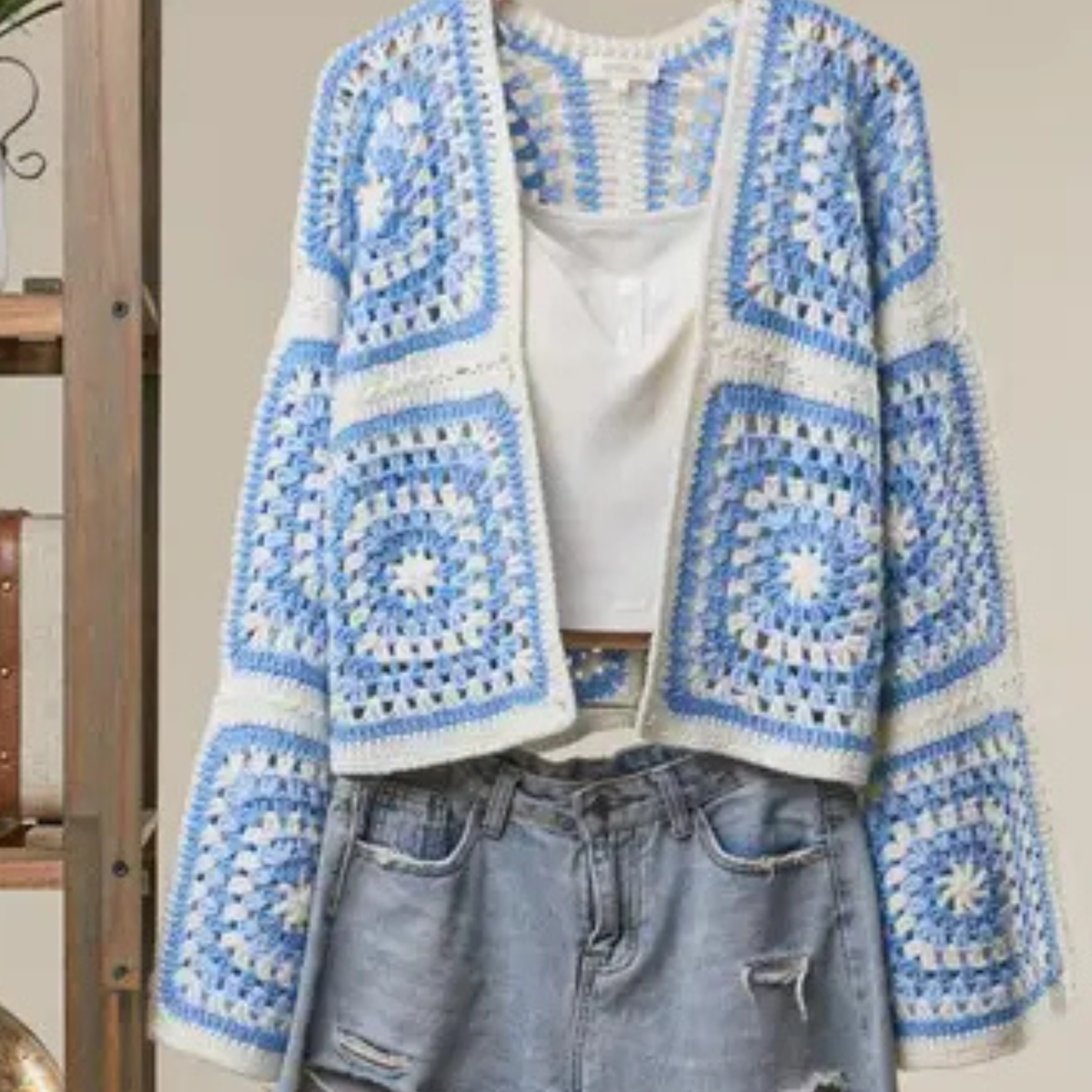 A cropped, open-front crochet cardigan with a blue and white granny-square pattern, styled over a white top and light-wash distressed jeans.