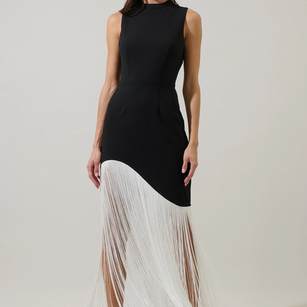 A sleeveless black dress with a high mock neck and a dramatic white fringe overlay on the lower half, shown on a model against a plain light beige studio background.