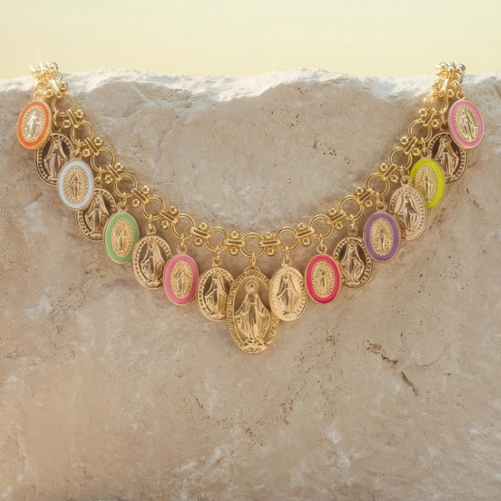 A gold-toned chain necklace featuring multiple oval Miraculous Medal charms in assorted pastel and bright colors, displayed draped over a light beige stone surface.