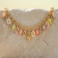 A gold-toned chain necklace featuring multiple oval Miraculous Medal charms in assorted pastel and bright colors, displayed draped over a light beige stone surface.