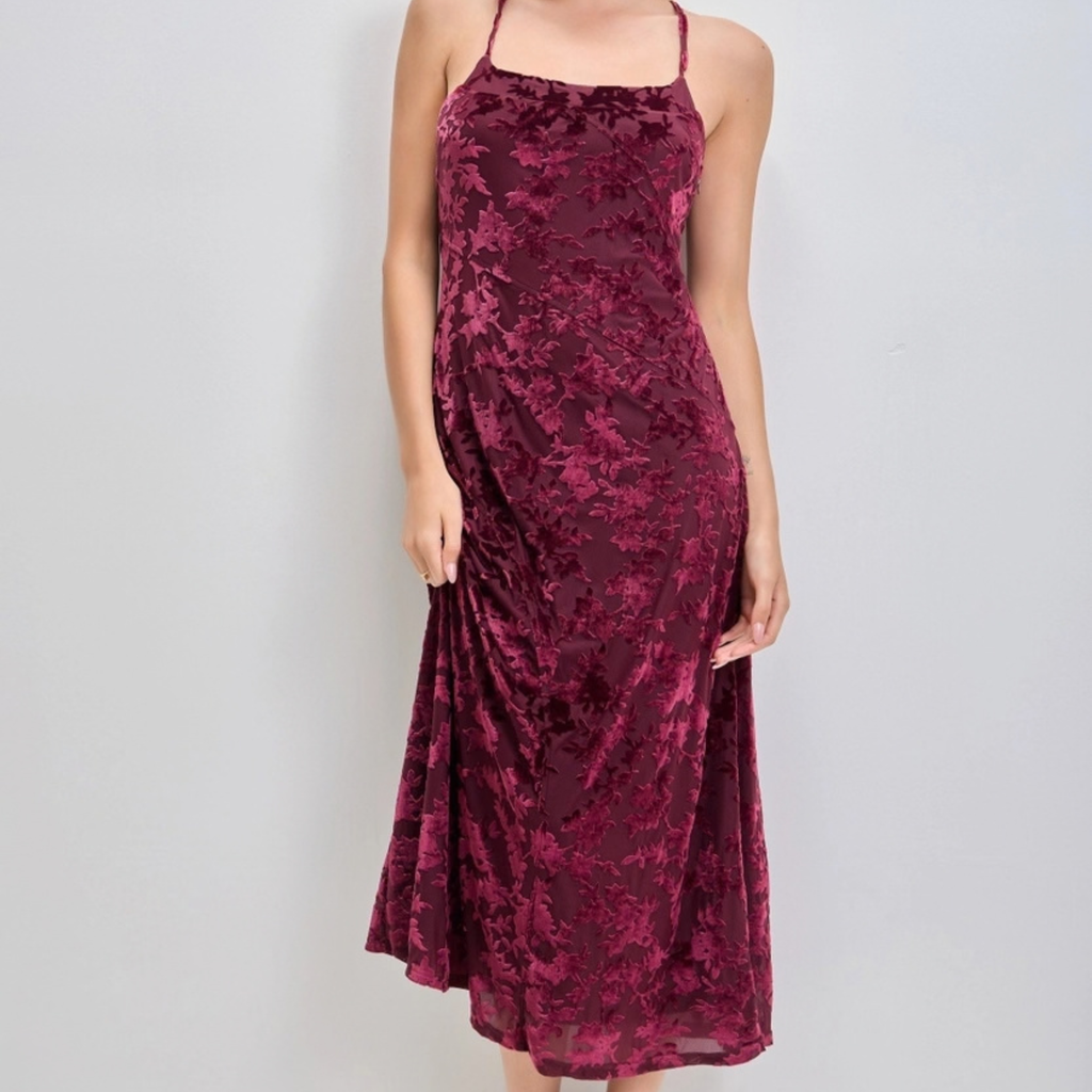 A woman wearing a sleeveless midi dress made of crushed velvet in a deep burgundy color, shown against a plain light gray background.