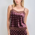 A woman wearing a burgundy velvet camisole pajama top with white polka dots and lace trim, paired with matching polka-dot pajama bottoms, against a light gray studio background.
