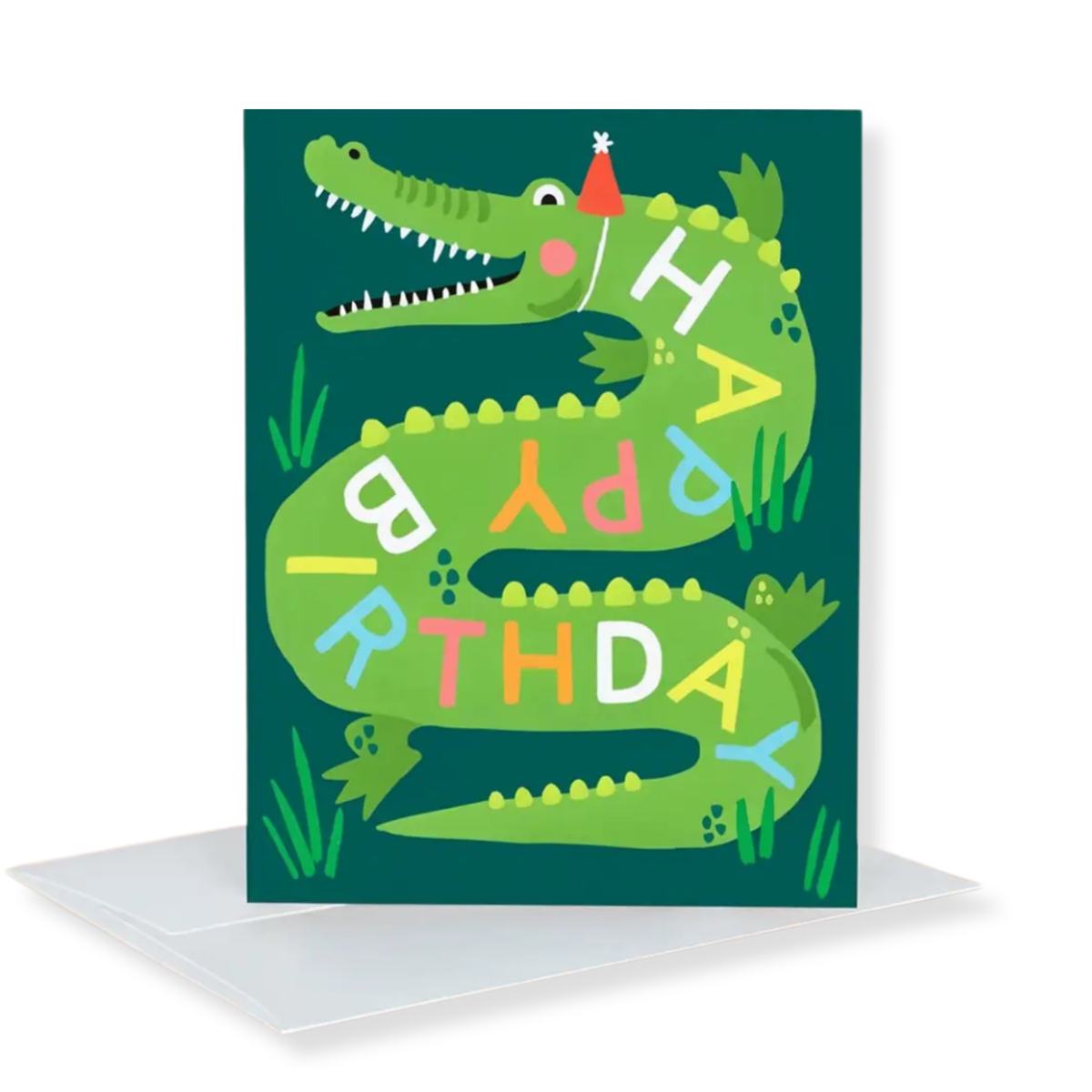 A green crocodile birthday card with colorful letters spelling 'HAPPY BIRTHDAY' and a small red party hat, shown standing upright with a white envelope behind it on a white background.