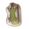 A pink ceramic serving platter shaped like a crocodile, featuring a green crocodile illustration with red eyes and claws, and a gold rim, shown on a white background.
