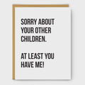 A white greeting card with bold black text reading 'SORRY ABOUT YOUR OTHER CHILDREN. AT LEAST YOU HAVE ME!' shown with a tan envelope behind it on a light gray background.