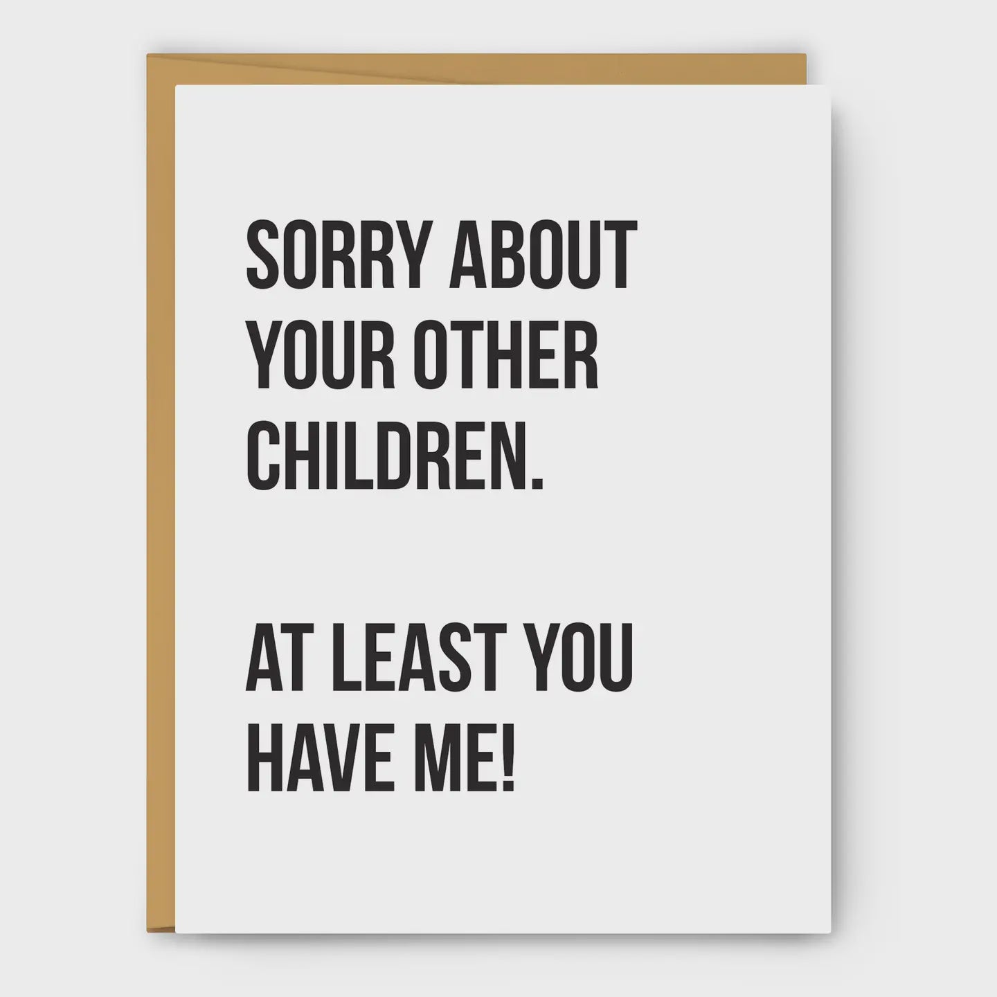 A white greeting card with bold black text reading 'SORRY ABOUT YOUR OTHER CHILDREN. AT LEAST YOU HAVE ME!' shown with a tan envelope behind it on a light gray background.